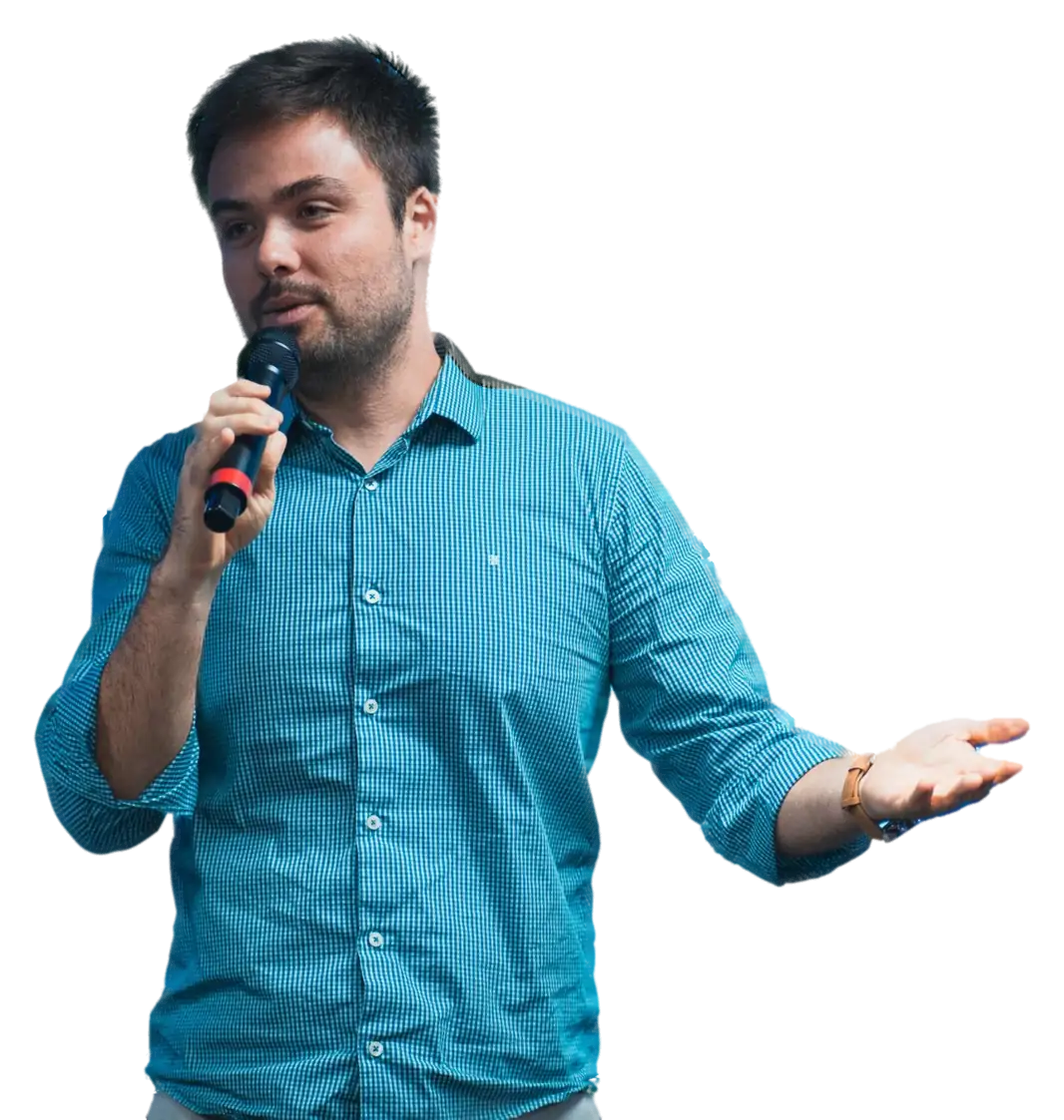 Minoru Raphael de camisa azul xadrez, falando ao microfone com o braço aberto Minoru Raphael de camisa azul xadrez, falando ao microfone com o braço aberto